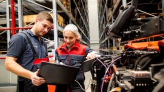 Två servicetekniker från Linde Material Handling tittar på en bärbar dator bredvid en truck.
