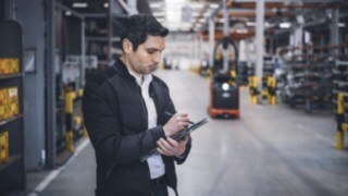 En medarbetare på Linde Material Handling står i lagerlokalen och gör anteckningar på sin surfplatta.