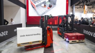Två truckar från Linde MH transporterar varor. En digital avbildning av truckarna visas på en skärm.