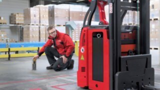 En Linde MH-anställd står på knä framför en L-MATIC och kontrollerar att allt stämmer.